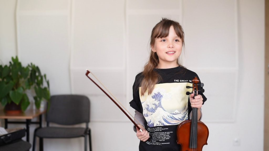 Zjęcie przedstawia dziewczynkę trzymającą skrzypce